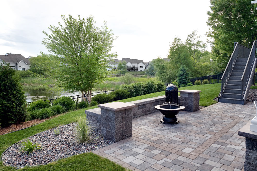 River rock mulch and small plants encompass the patio and incorporate elements of the existing landscaping, into the installation. A very small mulch divider keeps the river rock from being scattered about the yard. The freestanding wall, built with Standard units, adds seating for the fire pit.